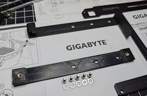 A rectangular 3D printed bracket with three holes to mount to the graphics card and two threaded heat-set inserts on each side to mount to the front of the case